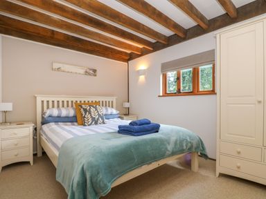 A bedroom with a bed with pillows and folded towels beside a window and a wardrobe at Oaklands Near Boscastle