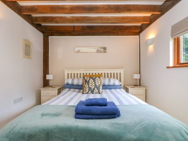 A bedroom with a bed blue towels on a green blanket wooden beams on ceiling and windows at Oaklands Near Boscastle
