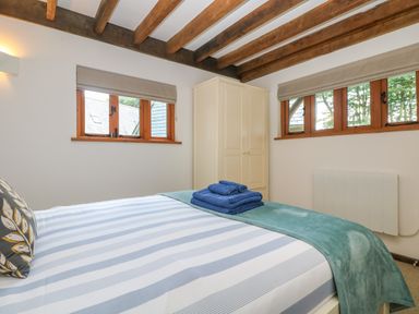 A bedroom with a bed striped bedding folded towels a wardrobe and wooden ceiling beams at Oaklands Near Boscastle
