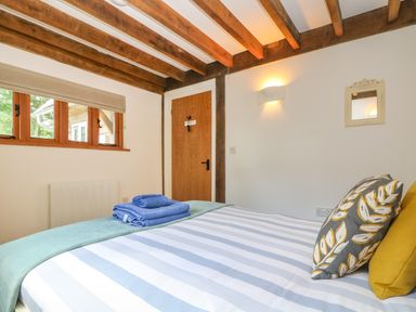 A bedroom with a bed with striped bedding blue towels on the bed wooden door and ceiling beams at Oaklands Near Boscastle
