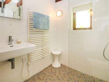A bathroom with a wall-mounted sink towel rack with a blue towel small white stool window and tiled floor at Oaklands Near Boscastle