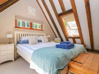 A bedroom with a bed pillows bedside tables lamps a window and wooden beams at Oaklands Near Boscastle