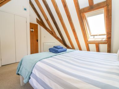 A bedroom with a striped bedspread folded towels wooden ceiling beams and a skylight window at Oaklands Near Boscastle