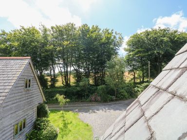 A view of trees and a gravel driveway next to wooden houses at Oaklands Near Boscastle