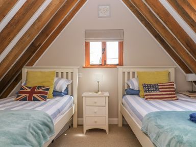 A bedroom with two single beds with striped bedding and pillows with flags and a window in between at Oaklands Near Boscastle
