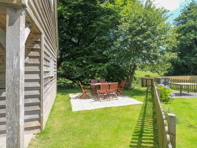 An outdoor patio area with wooden table and chairs on a tiled surface next to a wooden building and fenced garden at Oaklands Near Boscastle