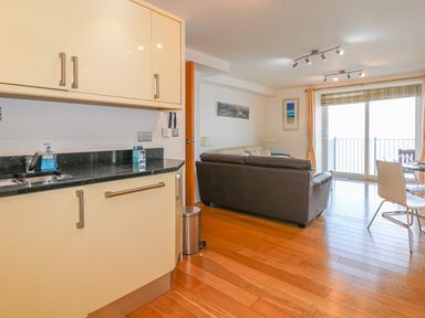 A kitchen and living area with cream cabinets brown sofa wooden floor and sliding glass door at Seasiders in Ilfracombe