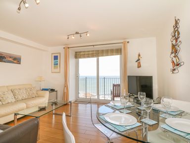 A living room with a glass dining table set for four and a sofa facing a glass coffee table with sea view at Seasiders Ilfracombe