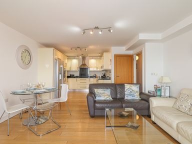 An open living and kitchen area with a dining table and chairs a brown and a white sofa and a glass coffee table at Seasiders Ilfracombe