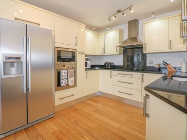 A kitchen with wooden floor cream cabinets black countertops stainless steel refrigerator oven and toaster at Seasiders in Ilfracombe