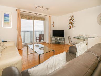 A living room with sofas glass coffee table dining table TV and balcony overlooking the sea at Seasiders Ilfracombe