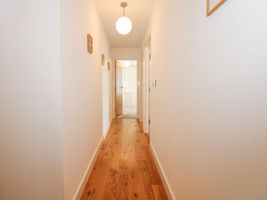 A hallway with wooden flooring and white walls with small framed pictures at Seasiders in Ilfracombe