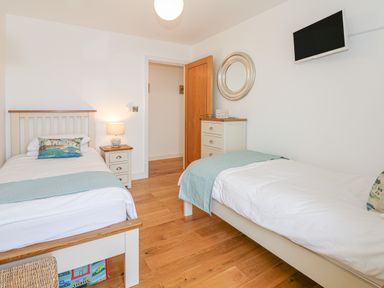 A bedroom with two single beds a wooden floor a wall mounted tv and a dresser with a round mirror at Seasiders in Ilfracombe
