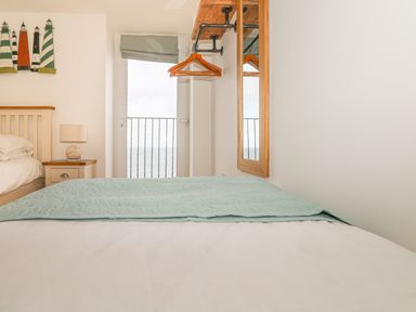 A bedroom with a bed a bedside table with lamp a wall mirror and a door with a balcony railing overlooking the sea at Seasiders in Ilfracombe