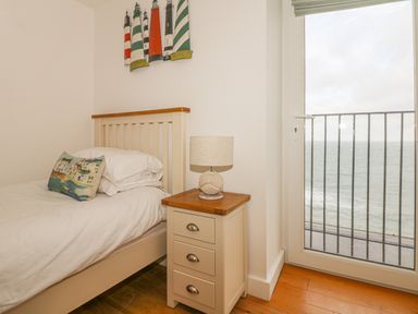 A bedroom with a single bed a bedside table with a lamp and a window overlooking the sea at Seasiders in Ilfracombe