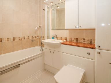 A bathroom with a bathtub shower sink toilet and storage cabinets at Seasiders in Ilfracombe
