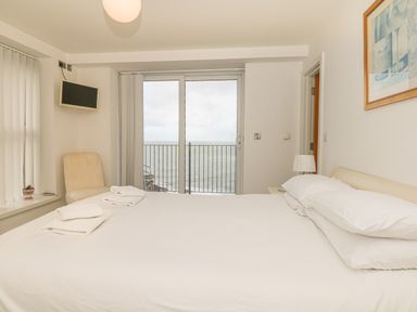 A bedroom with a bed and towels near a sliding glass door with a view of the sea at Seasiders Ilfracombe
