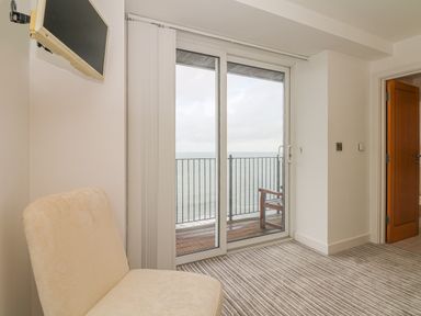 A room with a chair a wall-mounted television sliding glass doors leading to a balcony with ocean view at Seasiders Ilfracombe