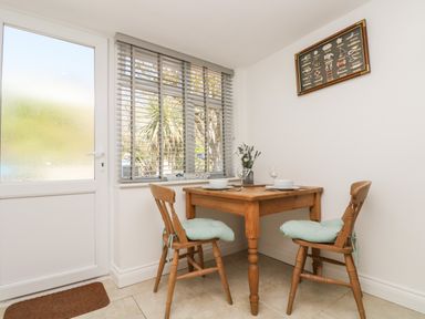 A small dining area with a wooden table and two chairs near a window and door at Seascape in Porthcurno