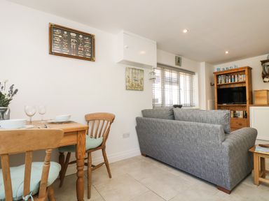 A dining table with chairs and a gray sofa next to a window in a living room at Seascape in Porthcurno