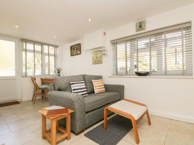 A living room with a gray sofa and striped cushions a small wooden table and a wooden stool with cushion at Seascape in Porthcurno