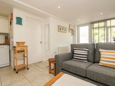 A living room with a gray sofa with striped pillows next to a white door and window with blinds at Seascape in Porthcurno