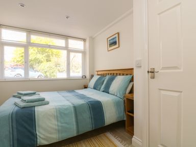 A bedroom with a double bed with blue striped bedding next to a window with blinds at Seascape in Porthcurno