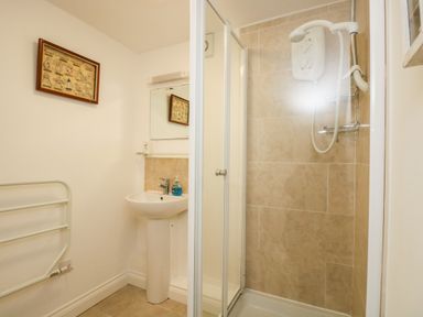 A bathroom with a shower enclosure a pedestal sink with a mirror and a towel radiator at Seascape in Porthcurno