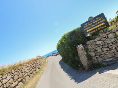 A road with stone walls on both sides and a parking area visible in the distance at Minack Theatre in Porthcurno