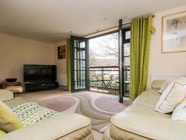 A living room with a television a beige sofa and open doors leading to a balcony at Riverview in Lostwithiel