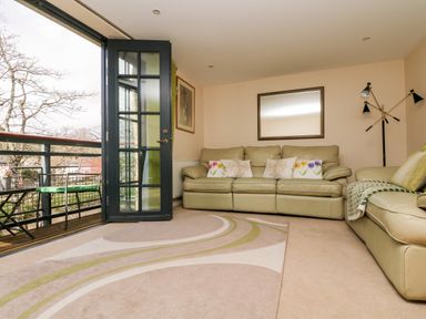 A living room with leather sofas rug and open door leading to a balcony at Riverview in Lostwithiel