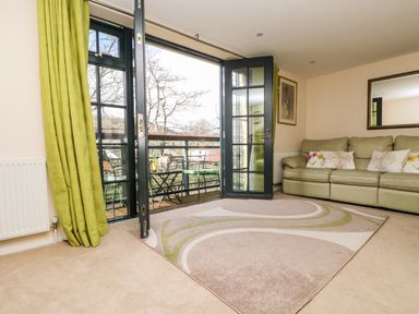 A living room with a green sofa and pillows a patterned rug and open glass doors leading to a balcony at Riverview in Lostwithiel