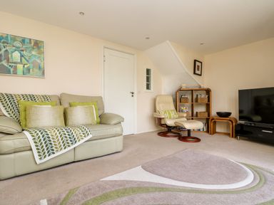 A living room with a sofa, armchair with footrest, bookshelf, television and rug at Riverview in Lostwithiel