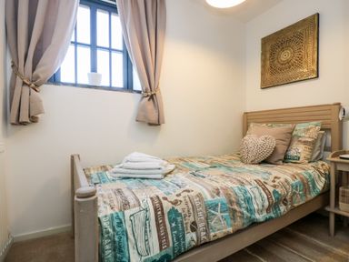 A small bedroom with a single bed featuring a patterned bedspread and pillows next to a window with curtains at Riverview in Lostwithiel