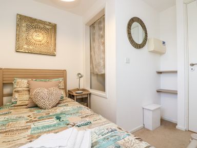 A bedroom with a single bed with patterned bedding and cushions a bedside table with a lamp a wall mirror and shelves at Riverview in Lostwithiel