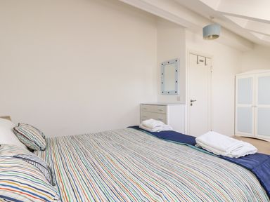 A bedroom with a bed with striped bedding a chest of drawers a mirror a door and a wardrobe at Riverview in Lostwithiel