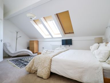 A bedroom with a bed sofa a chest of drawers floor lamp and skylight windows at Riverview in Lostwithiel