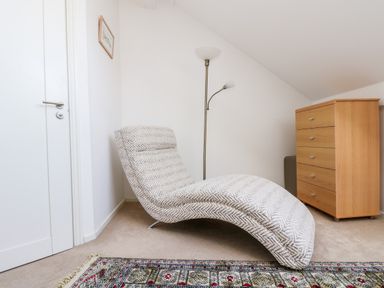 A curved lounge chair with a floor lamp and wooden chest of drawers in a room at Riverview in Lostwithiel