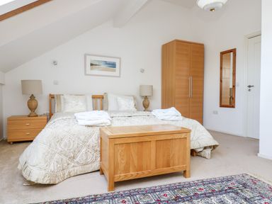 A bedroom with a double bed bedside tables table lamps a wooden trunk wardrobe a mirror and a patterned rug at Riverview in Lostwithiel