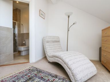 A lounge chair next to a floor lamp and dresser with a view into a bathroom at Riverview in Lostwithiel
