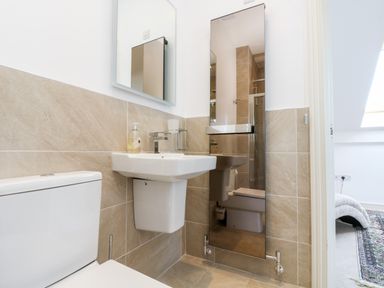 A bathroom with a toilet sink mirrors and beige tiles at Riverview in Lostwithiel
