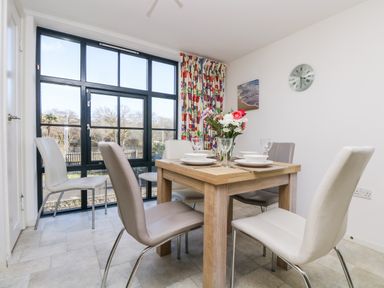A dining area with a wooden table set for four and chairs near large windows at Riverview in Lostwithiel