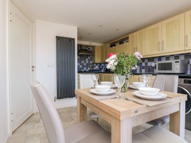 A kitchen with a dining table set with plates bowls glasses and flowers in a vase at Riverview in Lostwithiel