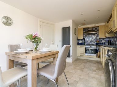 A dining table with plates and flowers in a kitchen with wooden cabinets and tiled backsplash at Riverview in Lostwithiel
