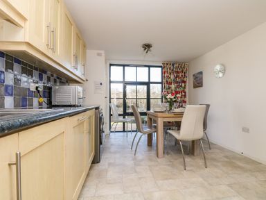A kitchen dining area with wooden cabinets a dining table and chairs and a large window at Riverview in Lostwithiel