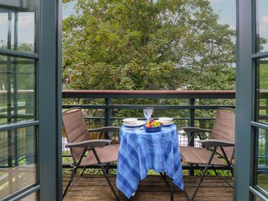 A small balcony with two chairs and a table covered with a blue checkered tablecloth with dishes and a bowl of fruit at Riverview in Lostwithiel