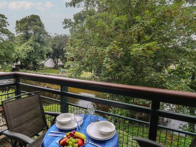 A balcony with a table set for two overlooking a river and trees at Riverview in Lostwithiel