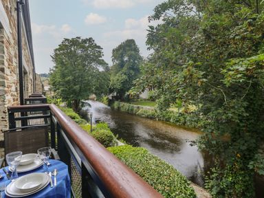 A balcony with a table set for dining overlooking a river with trees on each side at Riverview in Lostwithiel