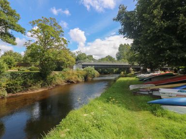 A river with boats on grass near a bridge and trees at Riverview in Lostwithiel