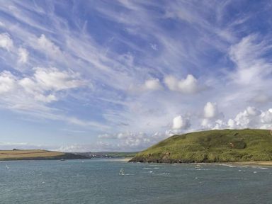 A coastal landscape with grassy hills and water under a sky with scattered clouds at Tides in Padstow